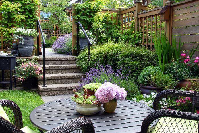 A small landscaped yard with flowers and greenery by wooden fencing by Thrive Landscape Services