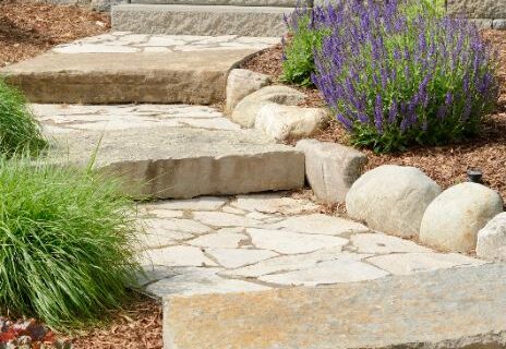 A walkway made of stones that leads to stairs by Thrive Landscape Services