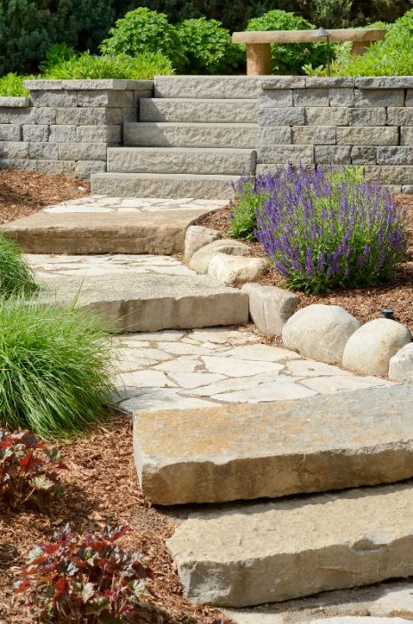 A walkway made of stones that leads to stairs by Thrive Landscape Services